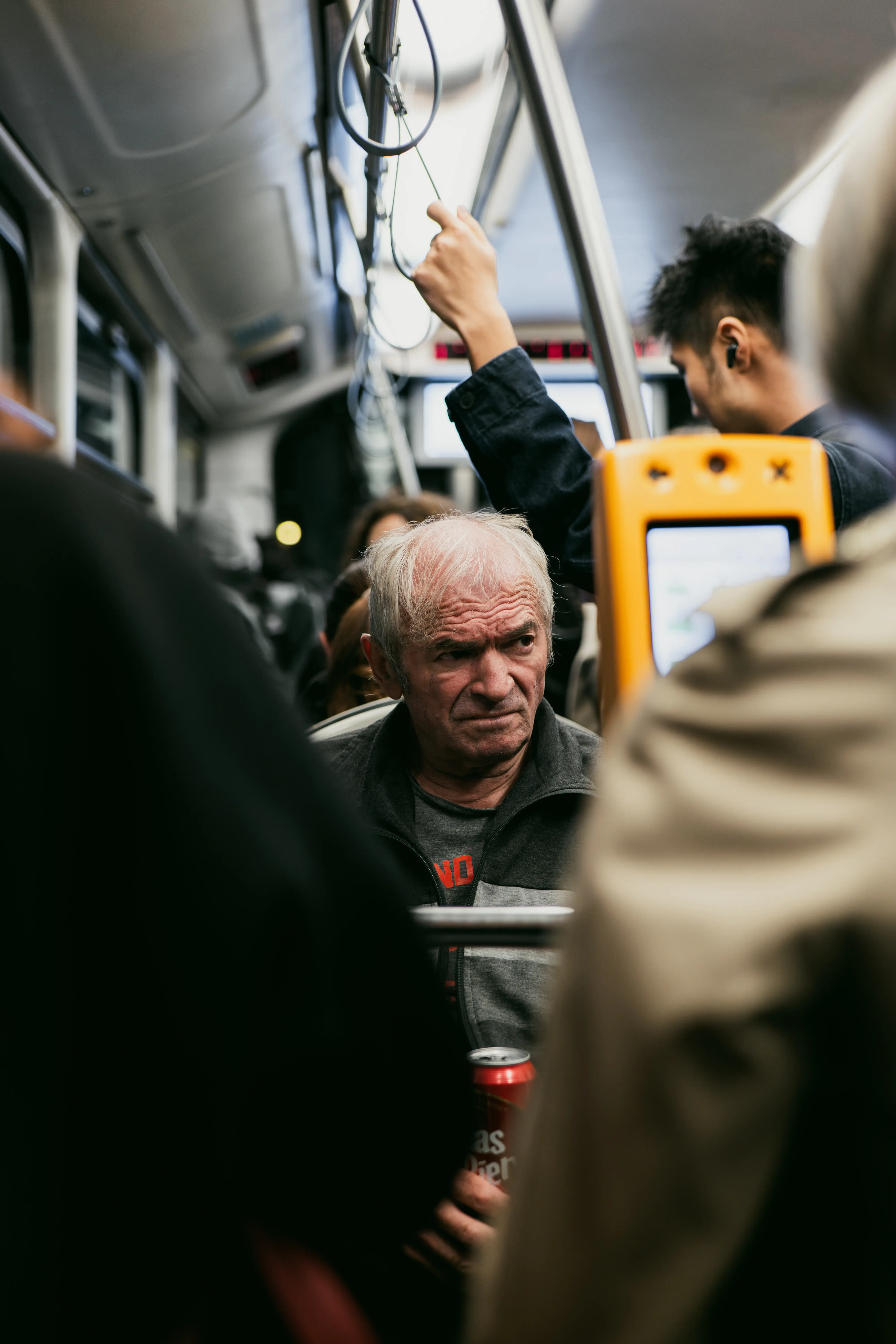 Zagreb tram interior with elderly passenger, orange validator and rush‑hour crowd in soft focus.